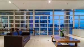 A spacious living area with a large window, a brown leather sofa, a wooden coffee table, and a vase with flowers. - Mercure Guarulhos Aeroporto Hotel (Guarulhos)