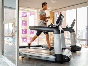 Ein Mann läuft auf einem Laufband in einem modernen Fitnessstudio mit großen Fenstern und Blick auf ein Schwimmbad.