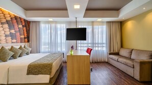 A hotel room with a bed, a desk with a TV, a sofa, and a stone wall. - Mercure Guarulhos Aeroporto Hotel (Guarulhos)