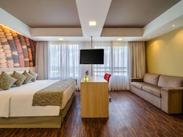 Una habitación de hotel con cama, escritorio con televisor, sofá y pared de piedra.