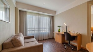 Habitación de hotel con sofá, escritorio con lámpara y vistas a través de cortinas traslúcidas.