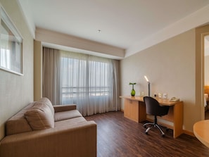 Habitación de hotel con sofá, escritorio con lámpara y vistas a través de cortinas traslúcidas.