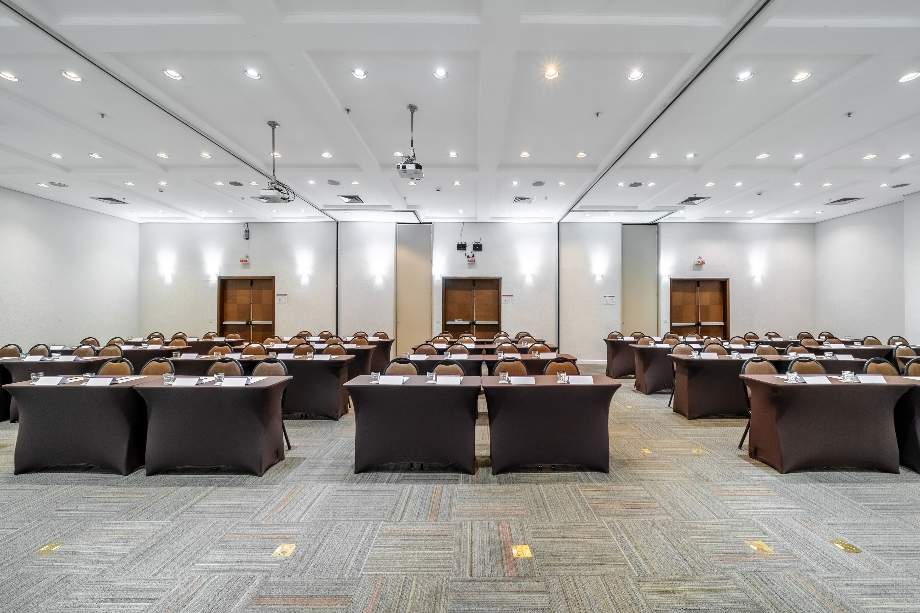 Un salón de conferencias con varias mesas y sillas, luces en el techo y un proyector.