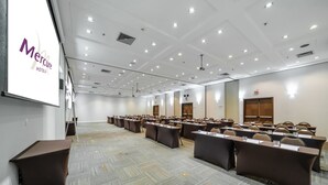 A conference room with rows of tables and chairs, a projector screen, and a white ceiling with recessed lighting. - Mercure Guarulhos Aeroporto Hotel (Guarulhos)