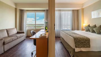 Ein Hotelzimmer mit Bett, Sofa, Schreibtisch mit Telefon und Fenster mit Vorhängen.