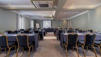 A conference room with multiple tables and chairs, equipped with water bottles and a projector screen.