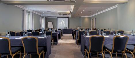 A conference room with multiple tables and chairs, equipped with water bottles and a projector screen.