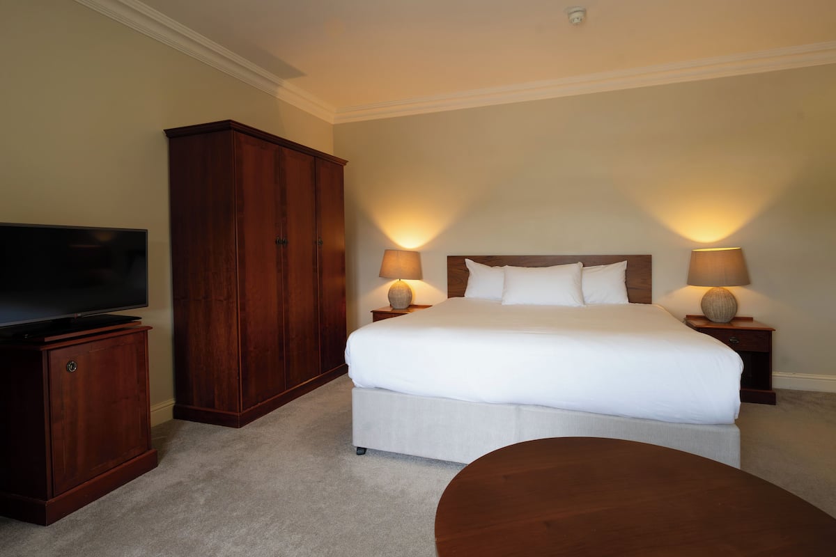 A hotel room with a large bed, two bedside lamps, a TV, a wooden wardrobe, and a round table.