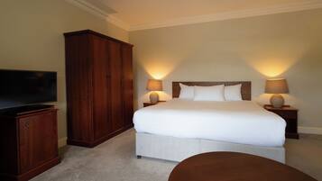 A hotel room with a large bed, two bedside lamps, a TV, a wooden wardrobe, and a round table.