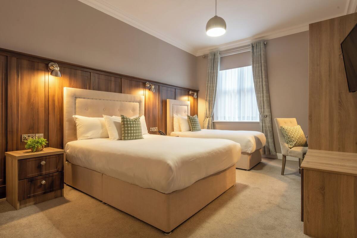 A hotel room with two beds, a nightstand, a chair, and a TV.