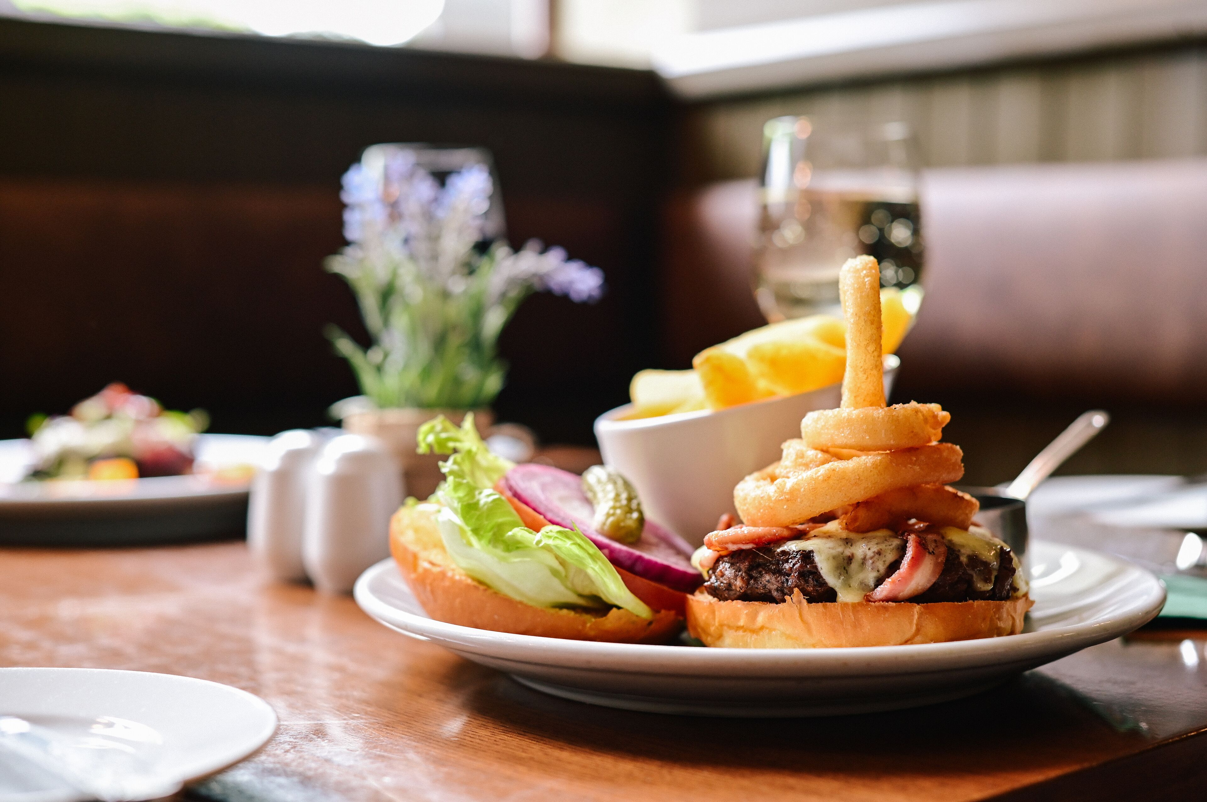 Een bord met een hamburger, uienringen en augurken op een houten tafel.