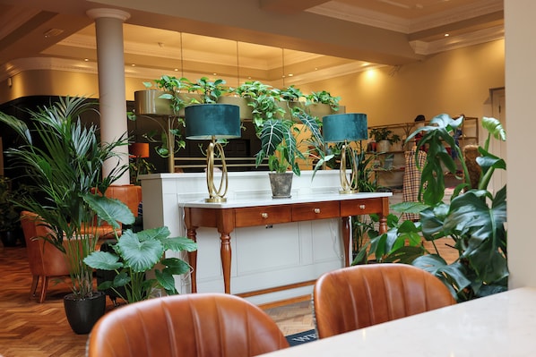 A hotel lobby with a wooden reception desk, leather chairs, and various potted plants. - Abbey Court (Nenagh)