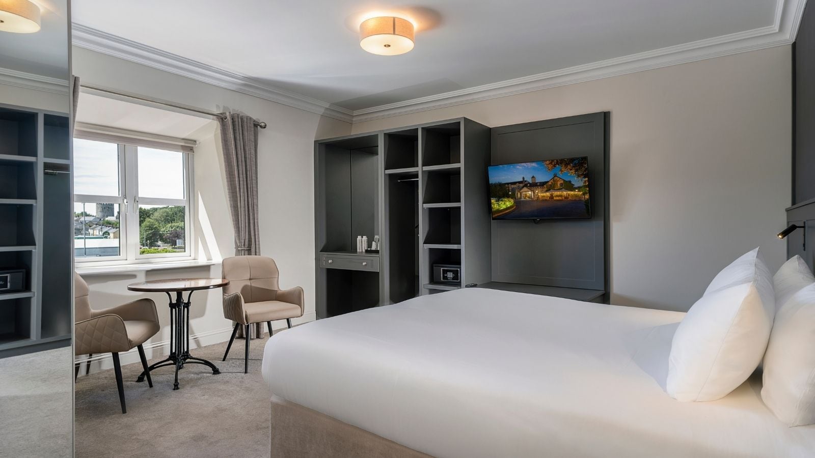 A hotel room with a bed, a desk, a chair, a TV, and a window with curtains.