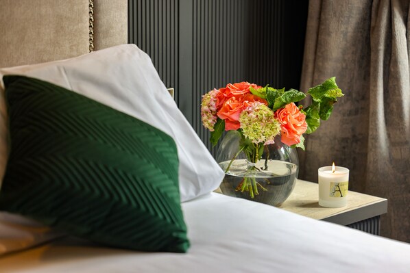 A neatly made bed with green and white pillows, a vase with flowers, and a candle on a bedside table. - Abbey Court (Nenagh)