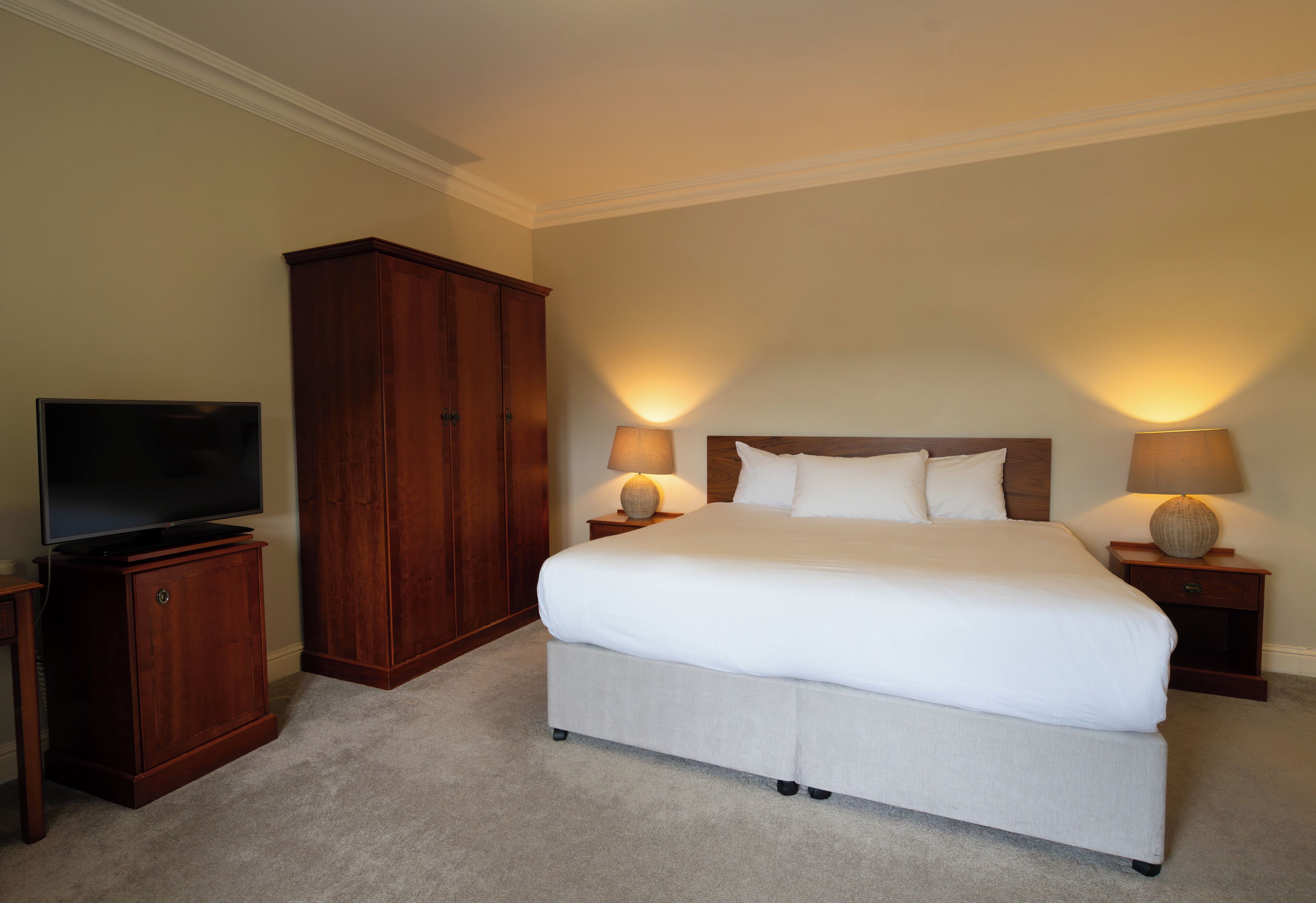 A bedroom with a large bed, two bedside lamps, a television, and a wooden wardrobe.