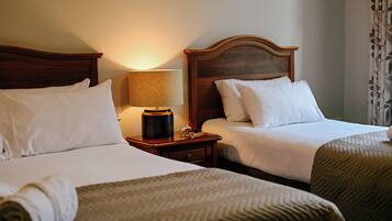 Una habitación de hotel con dos camas, una mesita de noche con lámpara y una ventana con cortinas.