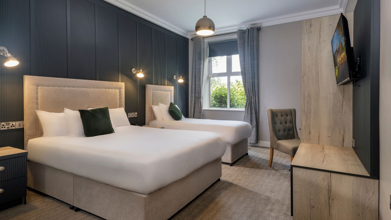 Une chambre d’hôtel avec deux lits, une chaise, un téléviseur et une fenêtre avec des rideaux.
