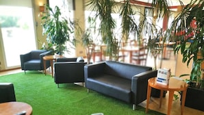 Een zithoek met een vloer van groen kunstgras, zwarte leren banken, houten tafels en potplanten.