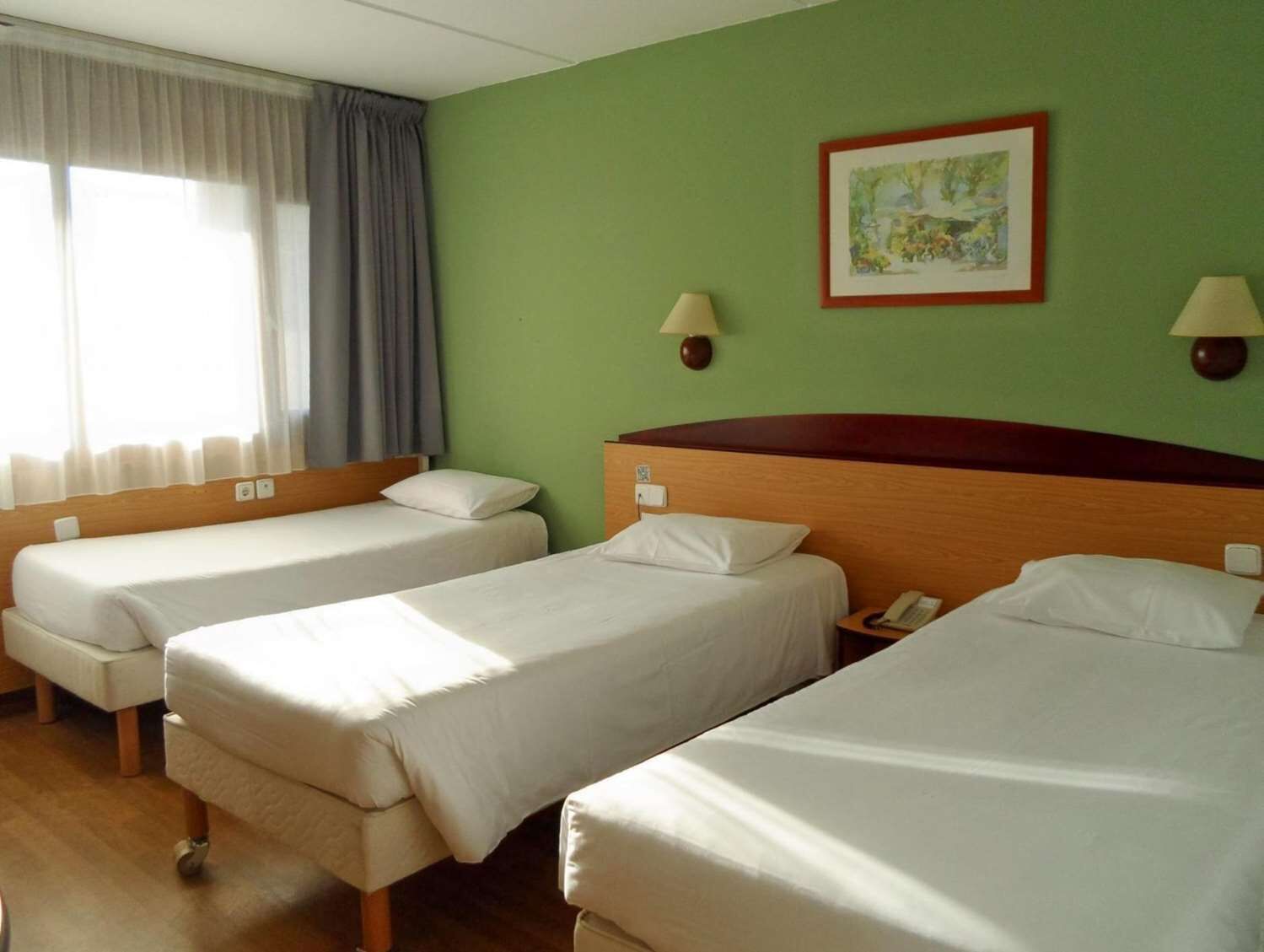 A hotel room with two single beds, a wooden headboard, a green wall, and a framed picture.