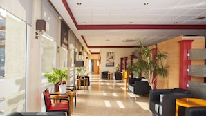 Een hotellobby met een lange gang, zithoeken en grote ramen.