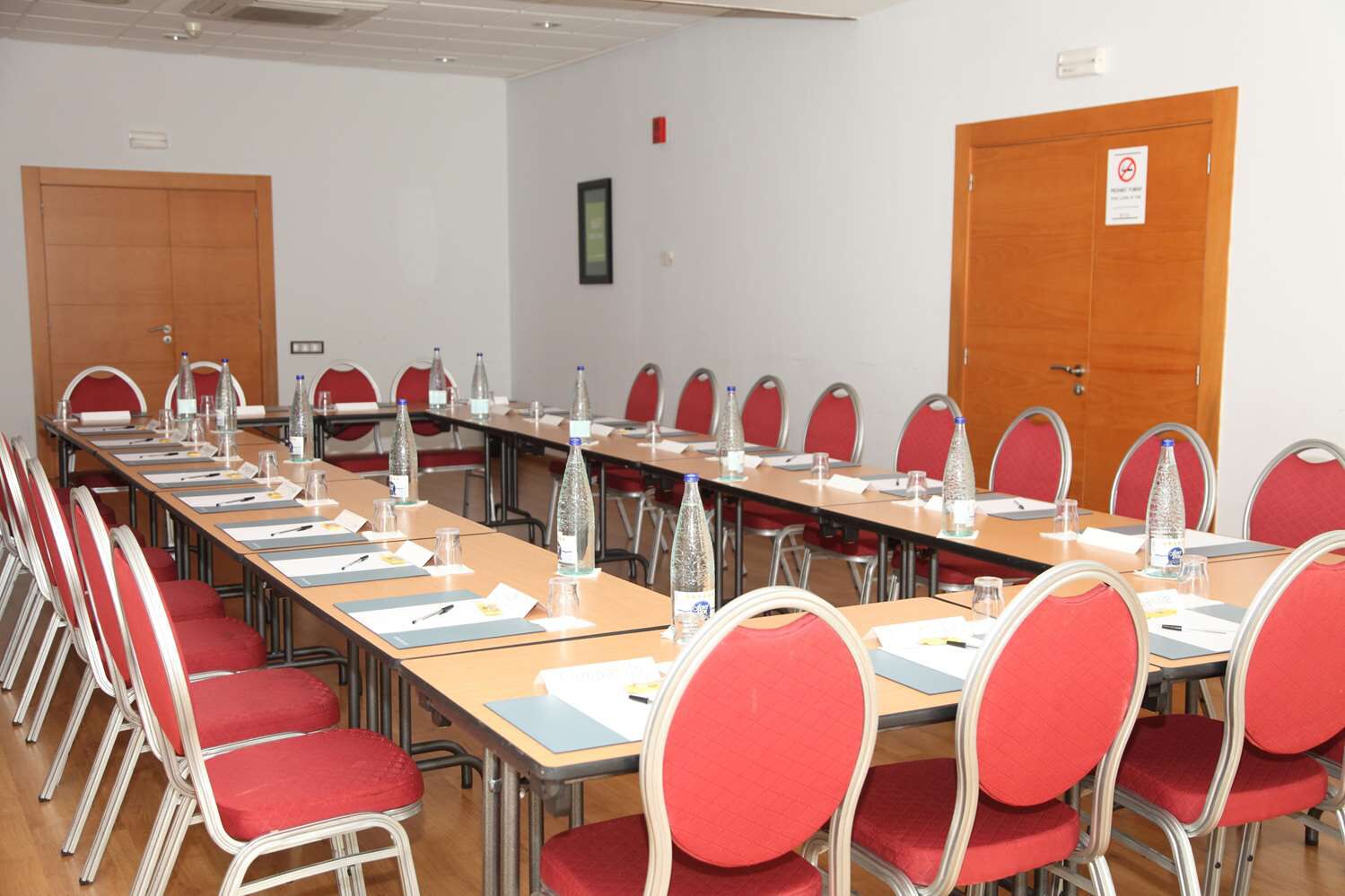 Une salle de conférence avec une longue table, des chaises rouges, des bouteilles d’eau et des documents.