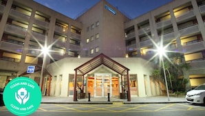 Een meerlaags hotel met een centrale ingang, een bordje dat een taxidienst aangeeft, en een 'Clean and Safe' logo.