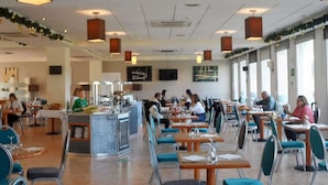 Een ruime eetzaal met hoge plafonds, moderne verlichting en een centraal buffet.