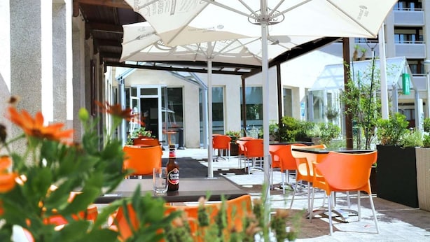 Een terras met oranje stoelen en witte parasols, een fles Estrella Galicia bier en een glas op een tafel.