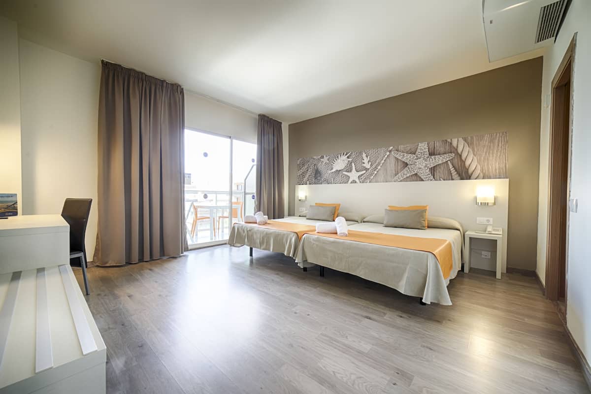 A hotel room with two beds, a desk, and a large window with curtains.
