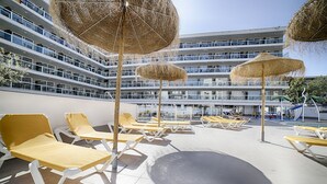 En takterrass med solstolar och parasoller av halmtak, med utsikt över en modern byggnad med flera balkonger.