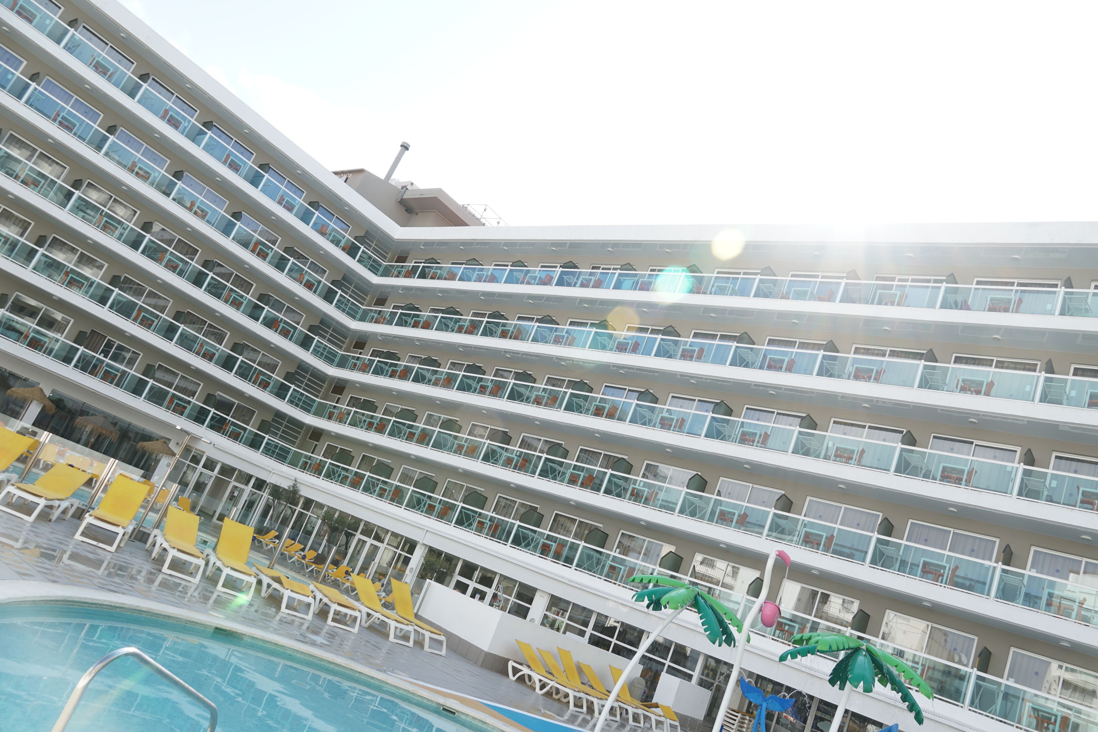Ein mehrstöckiges Hotel mit Balkonen, einem Poolbereich inklusive Liegestühlen und tropischer Dekoration.