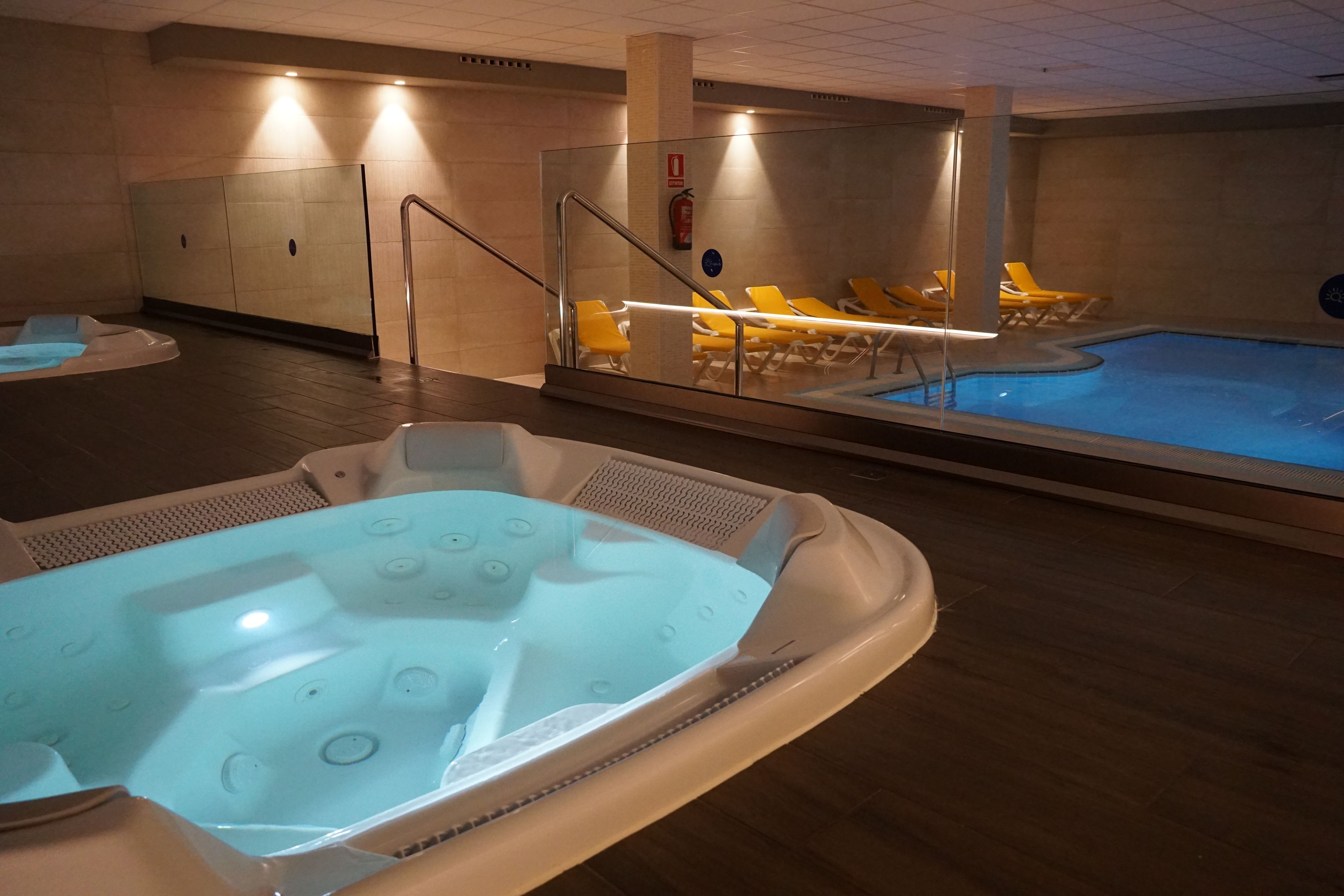 Zona d'spa amb dues banyeres d'hidromassatge i una piscina, equipada amb gandules i un extintor.