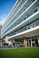 Un immeuble moderne à plusieurs étages, doté de balcons, avec un espace verdoyant devant et des vélos garés à l’extérieur.