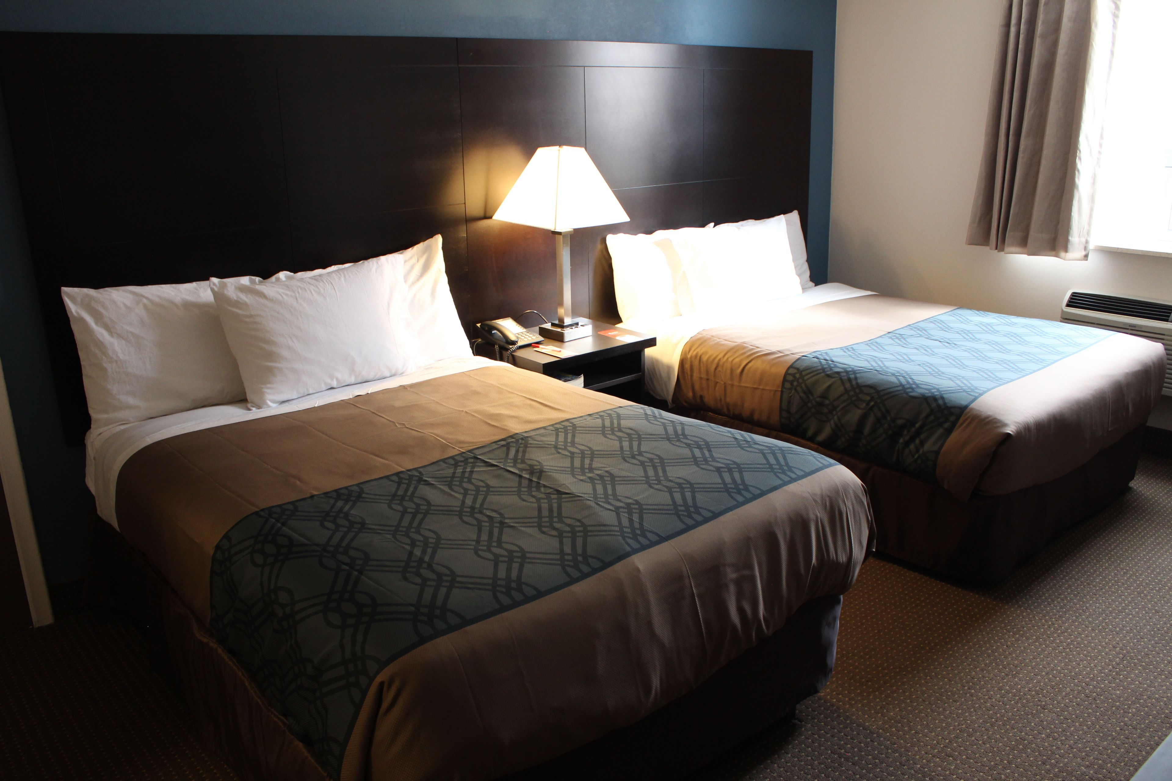 Quarto de hotel com duas camas, uma mesa de cabeceira com abajur e uma janela com cortinas.