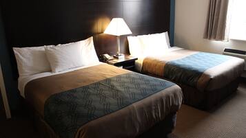 Quarto de hotel com duas camas, uma mesa de cabeceira com abajur e uma janela com cortinas.