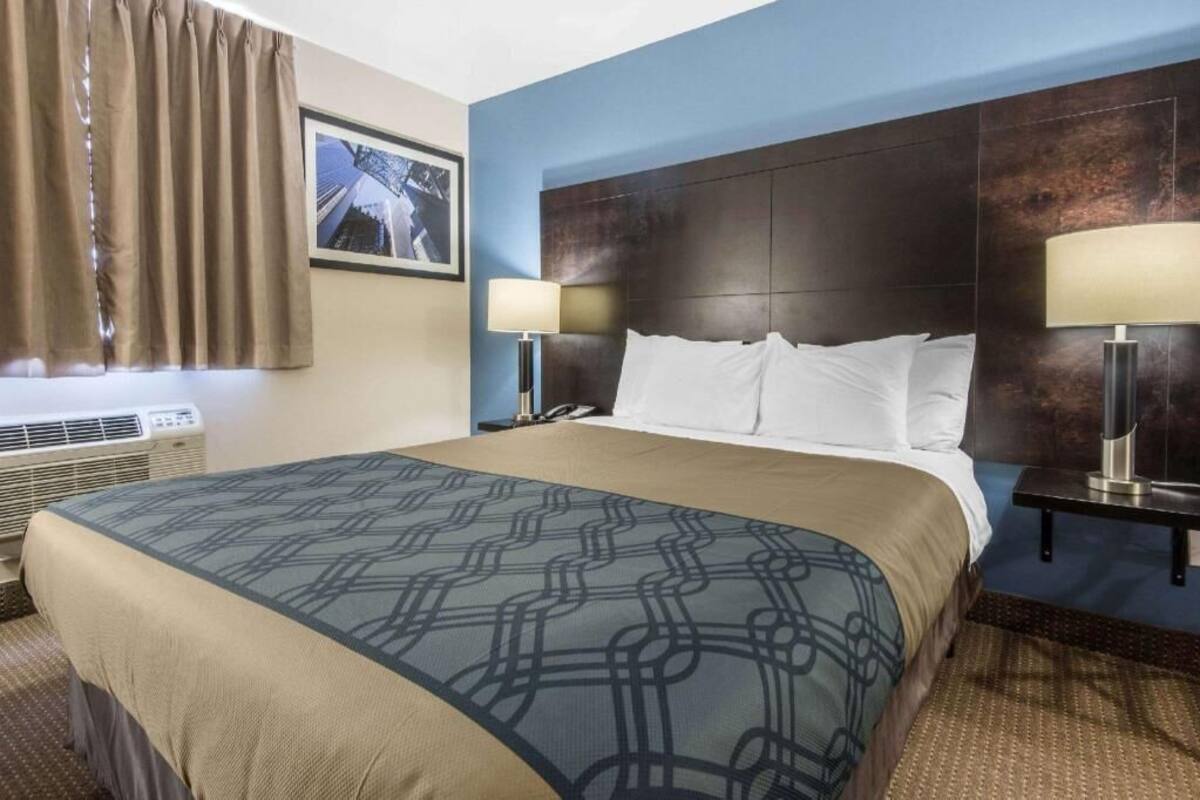 A hotel room with a large bed, two bedside lamps, a framed picture on the wall, and a window with curtains.