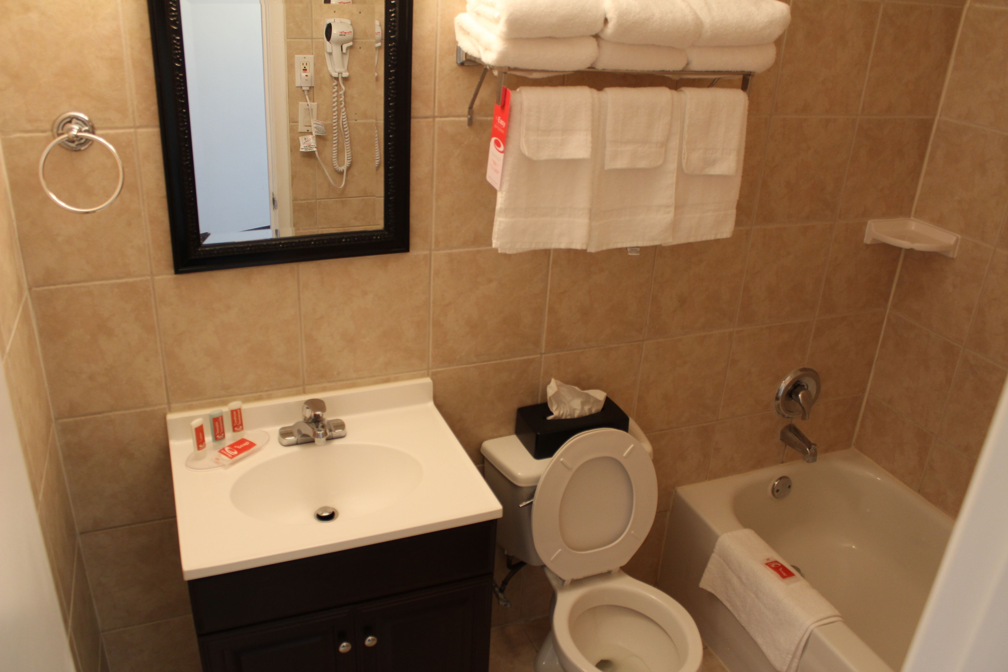 A bathroom with a sink, toilet, and bathtub. There are towels and a hand dryer on the wall.
