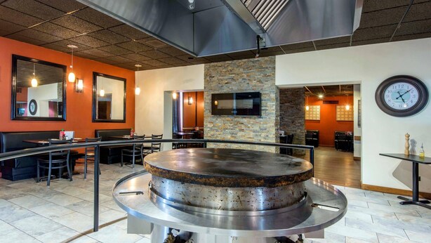 A restaurant with a large central grill, seating area, and a clock on the wall. - Econo Lodge (Sudbury)