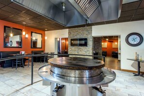 A restaurant with a large central grill, seating area, and a clock on the wall. - Econo Lodge Sudbury West (Sudbury)