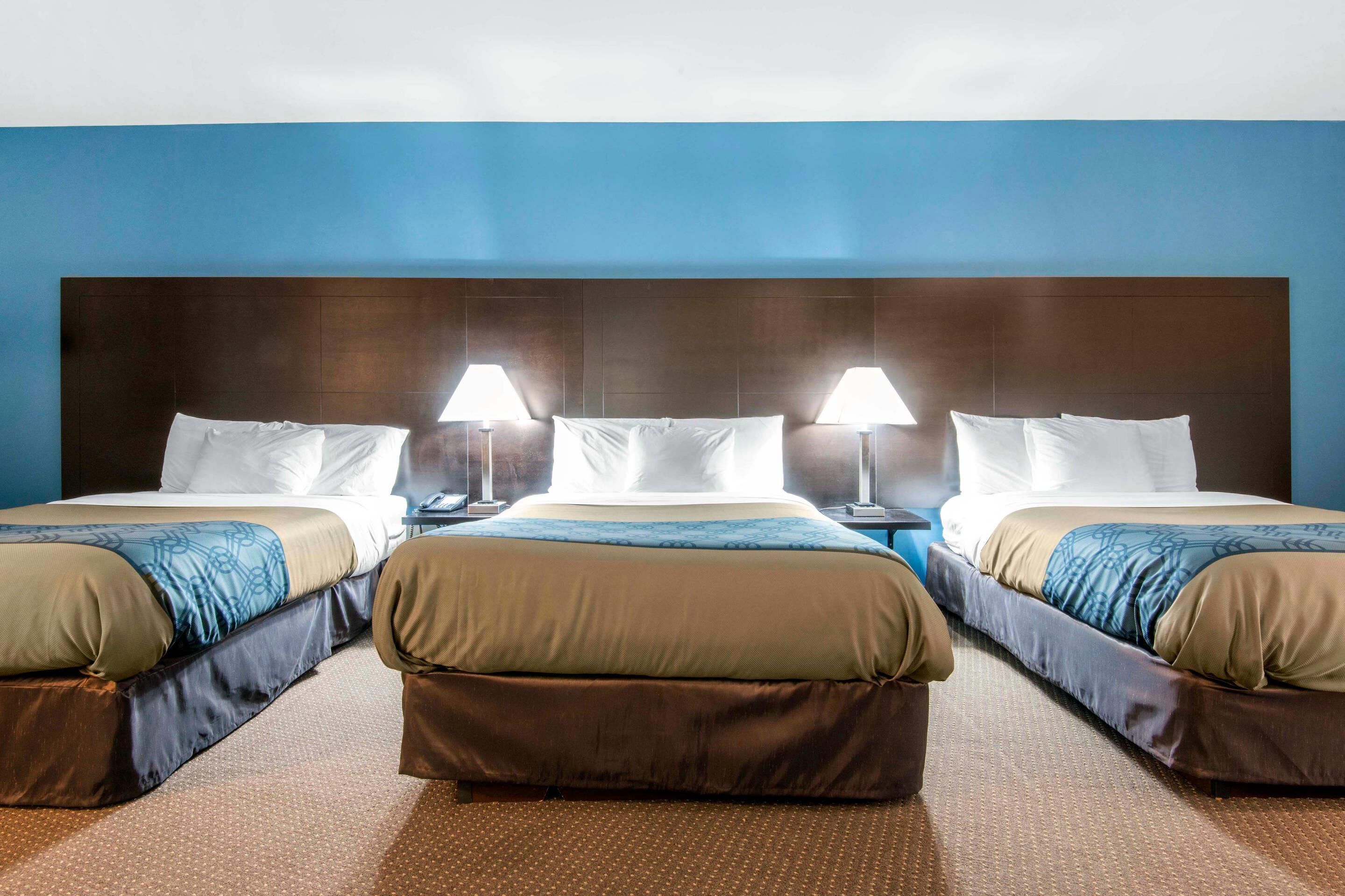 Una habitación de hotel con tres camas, cada una con cabecera, mesitas de noche y lámparas.