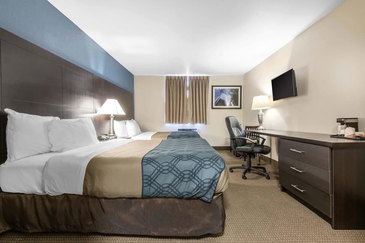 A hotel room with a large bed, a desk with a chair, a television, and a window with curtains.