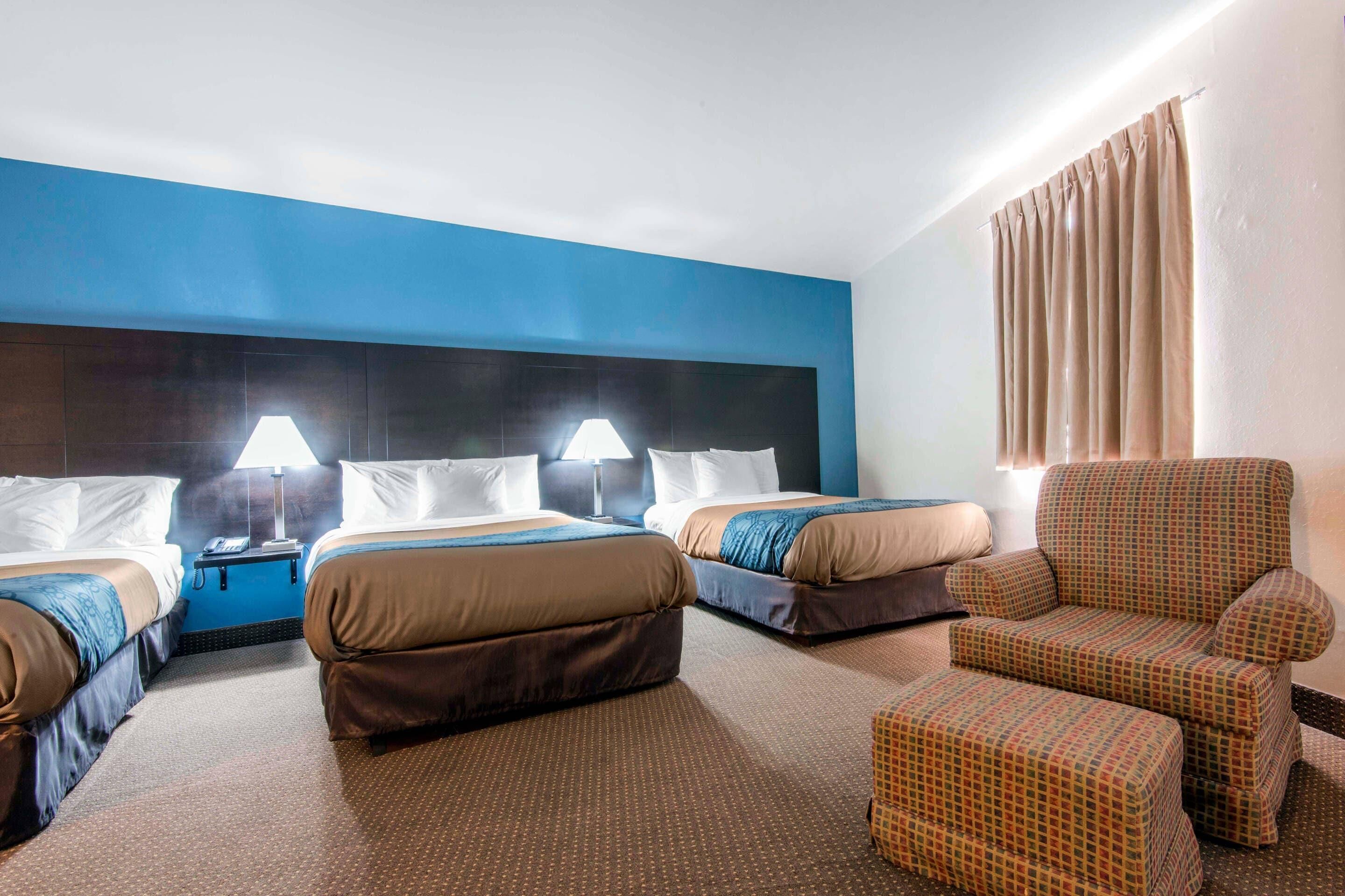 Une chambre d’hôtel avec deux lits, une chaise, une table de chevet et une lampe.