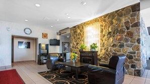 A modern living room with a stone accent wall, a flat-screen TV, a fireplace, and a dining area with a table and chairs. - Econo Lodge (Sudbury)