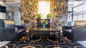 A room with a stone wall, two leather chairs, a table with a vase of sunflowers, and a sign indicating a lounge area. - Econo Lodge (Sudbury)