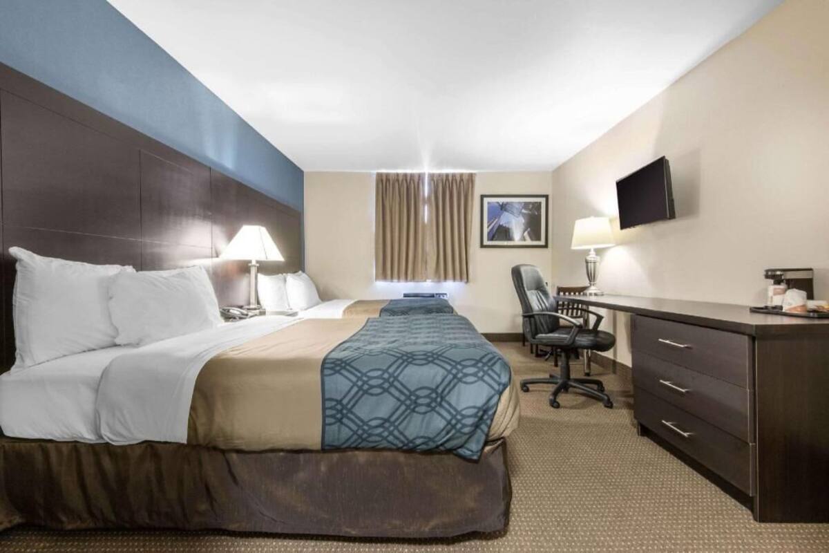 A hotel room with a large bed, a desk, a chair, a television, and a window with curtains.