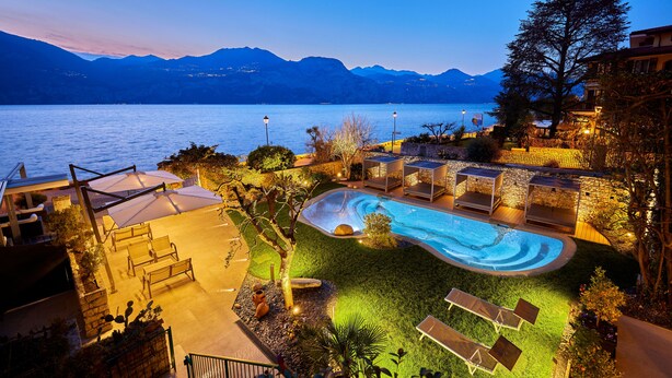 Una piscina con sillones de descanso y vistas a un lago y montañas al anochecer.
