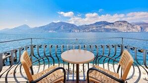Una terraza con una mesa redonda y cuatro sillas de mimbre, con vistas a una masa de agua y una costa montañosa.
