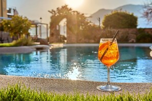 A glass of orange drink by a pool with a clear view of the pool and surrounding greenery. - Lake Front Hotel Brenzone (Brenzone sul Garda)
