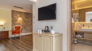 Una habitación de hotel moderna con una pared de acento de piedra, un televisor de pantalla plana, un armario de madera, una silla y un baño con espejo y lavamanos.