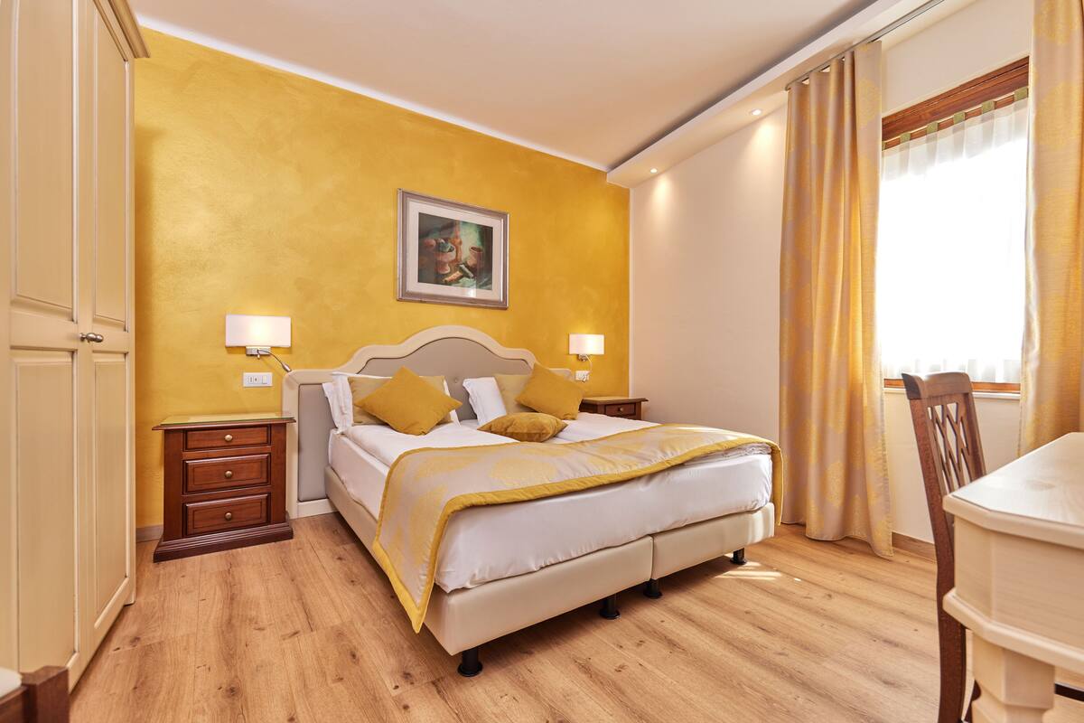 Habitación de hotel con cama, mesitas de noche, un sillón y un cuadro en la pared.